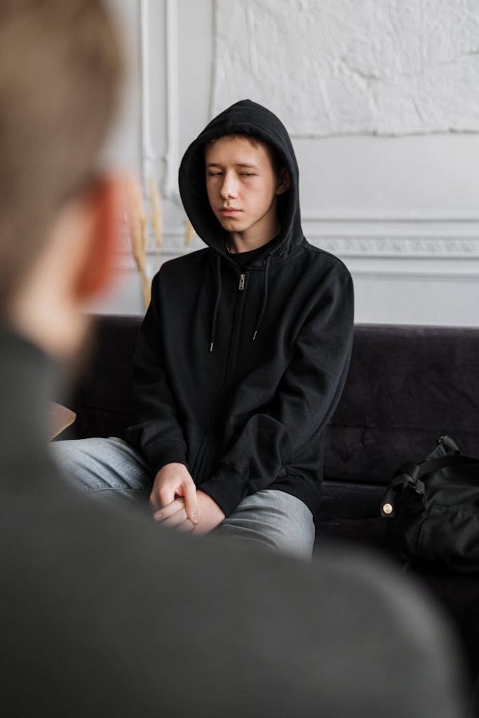 pexels photo 4100434 A teenager in a black hoodie engages in a counseling session, sitting calmly indoors.